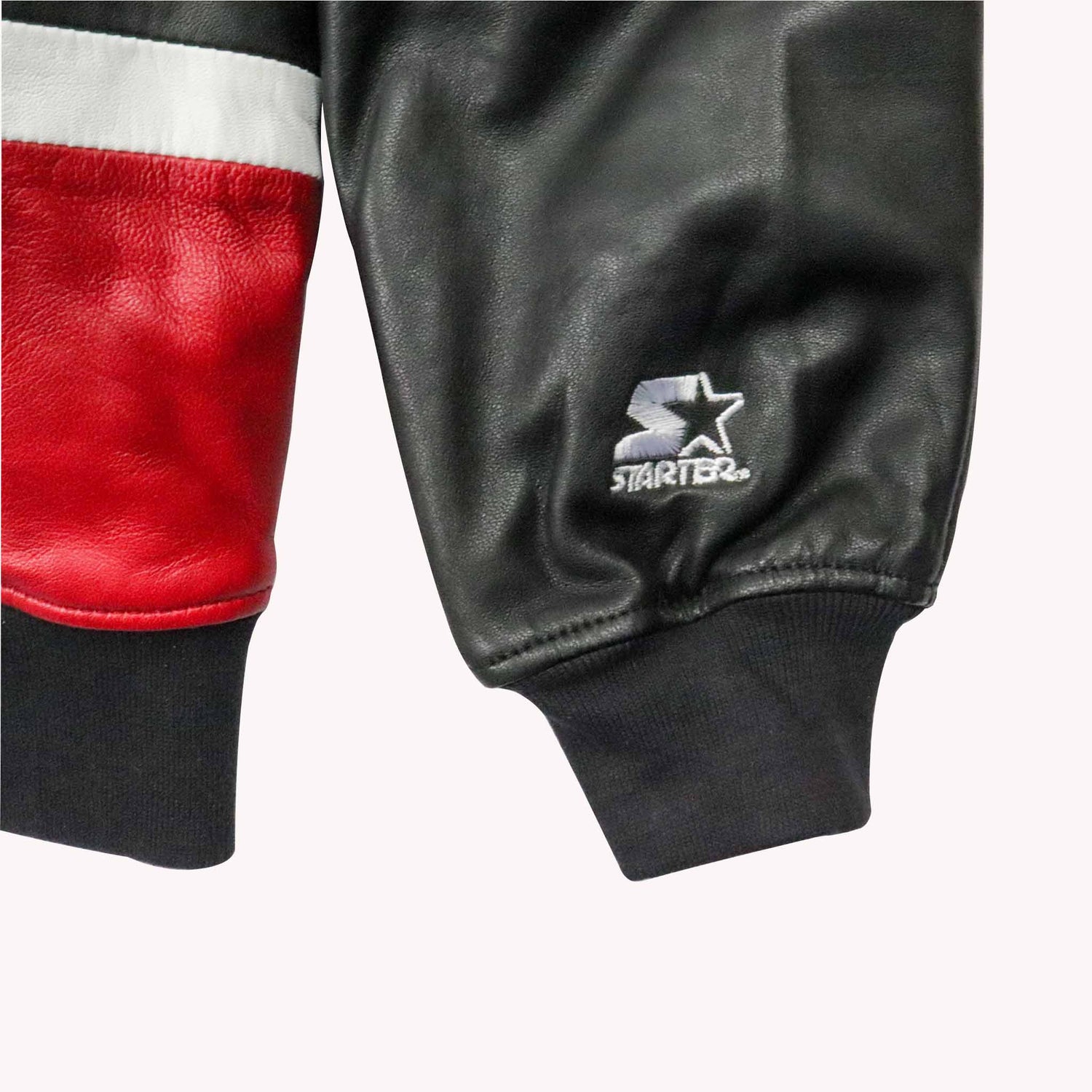 Close-up of a black leather jacket with a visible Starter logo on a white background